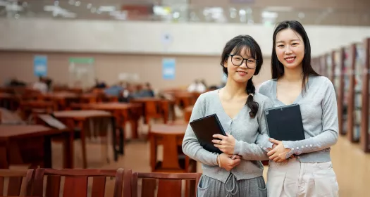 Two students holding books in a library